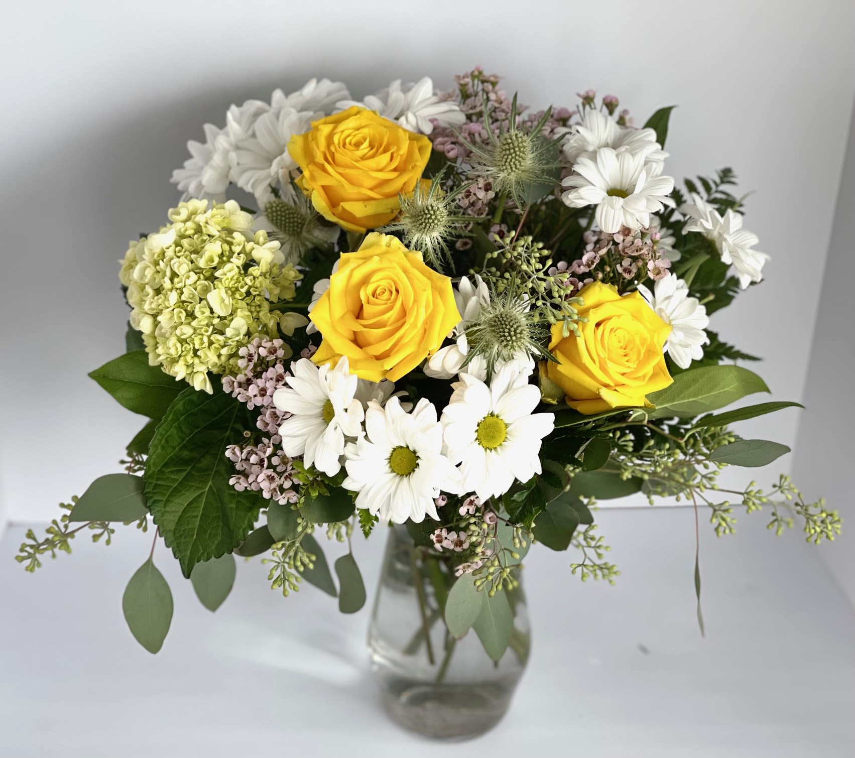 Yellow roses and white daisies in a clear glass vase