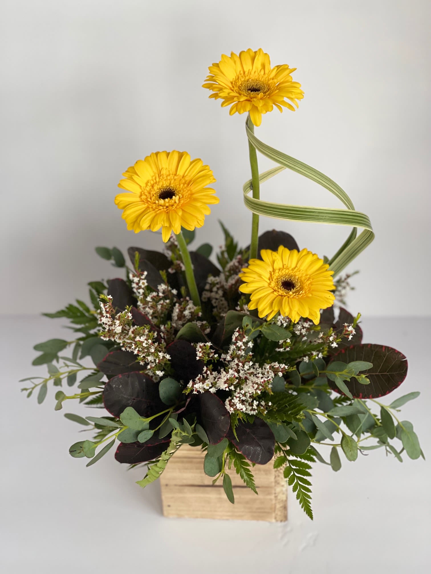 Yellow gerbera daisies in a wooden box with mixed greenery