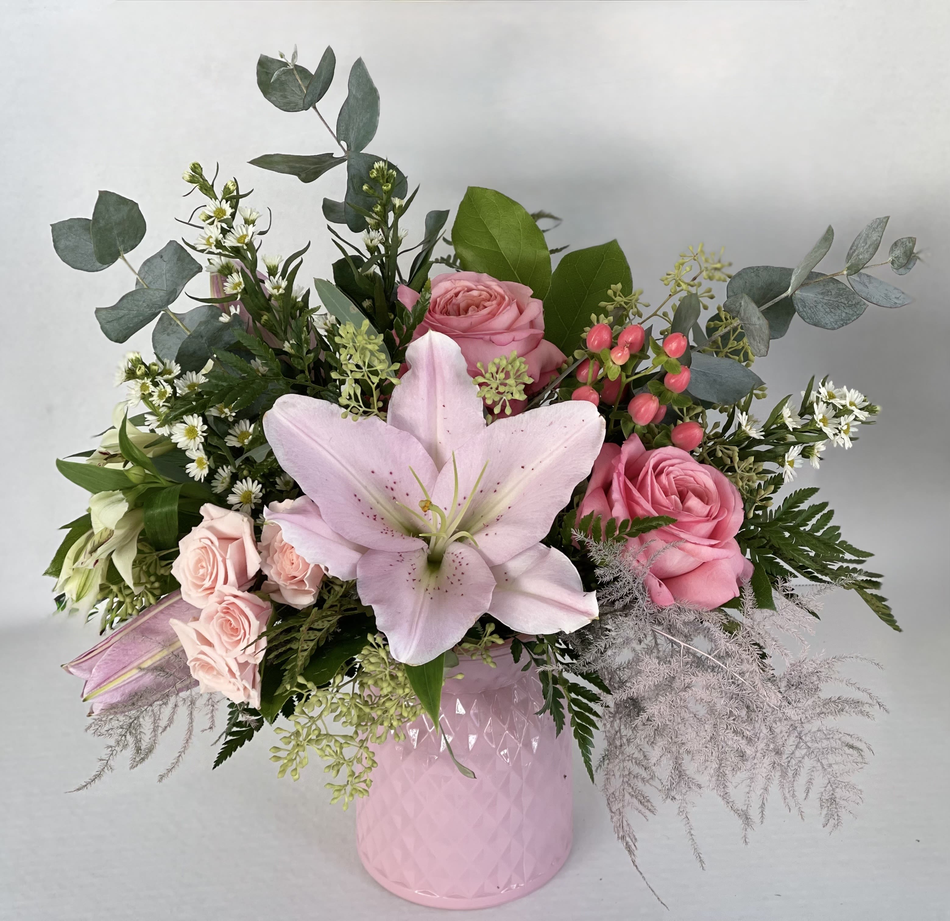 Pink roses and a pale lily arranged in a pink vase