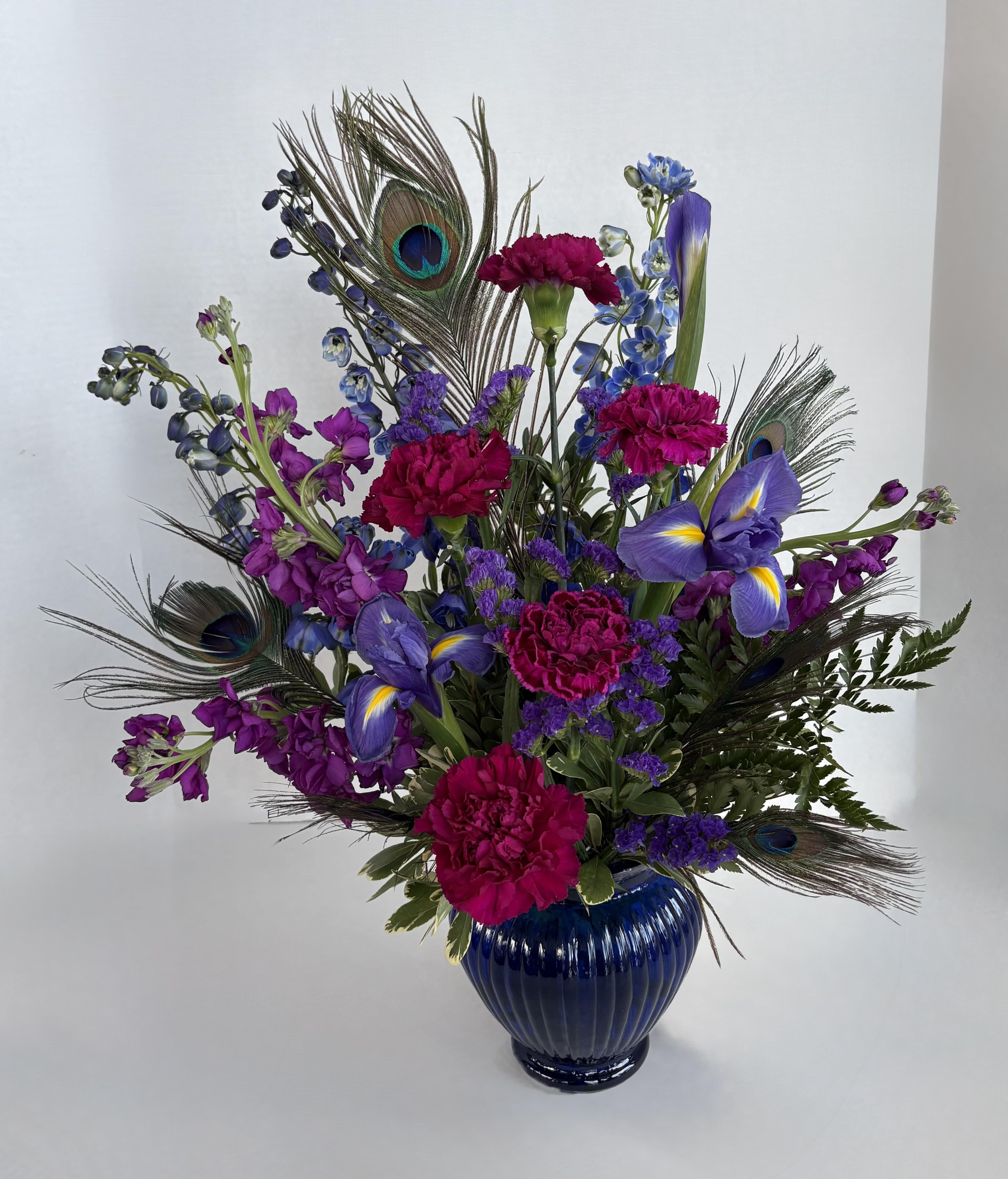 Purple and pink floral arrangement in a blue vase with peacock feathers