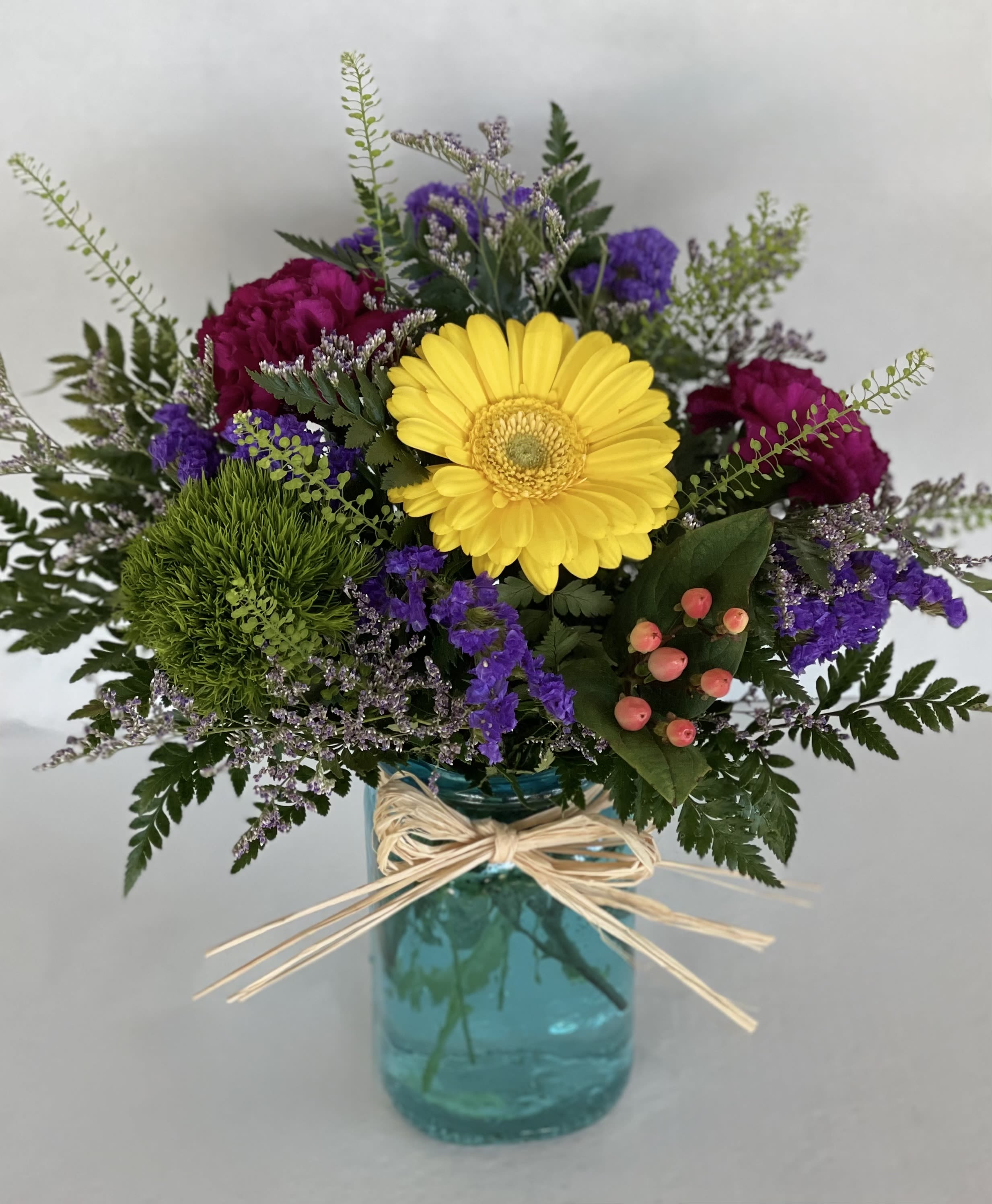 Mixed bouquet with a yellow gerbera daisy in a blue glass vase