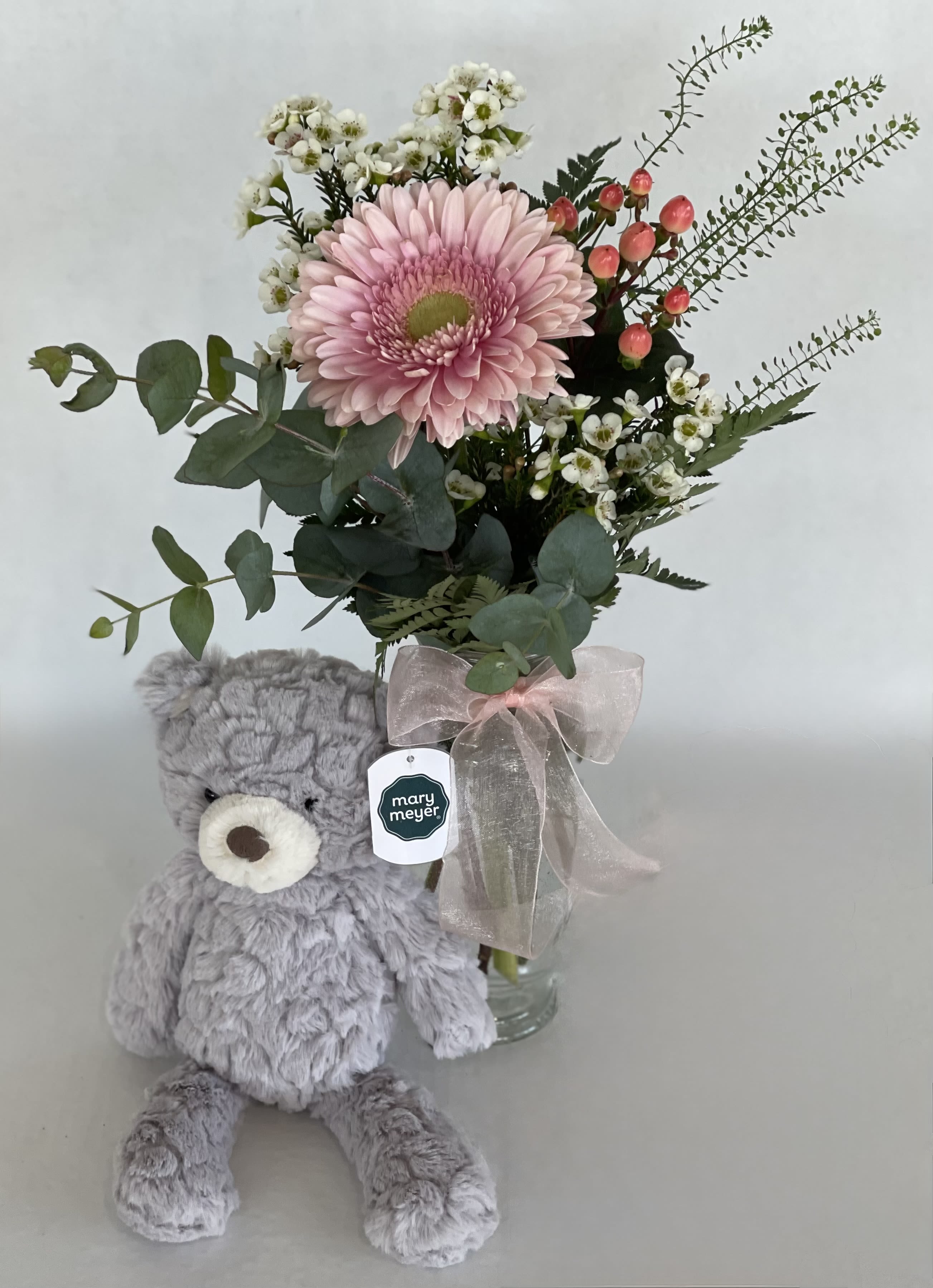 Pink gerbera bouquet in a glass vase with a gray teddy bear