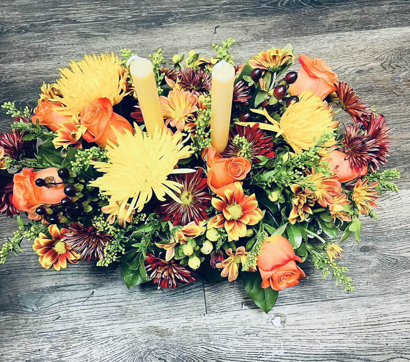 Oval floral centerpiece with orange roses, yellow mums, and two taper candles