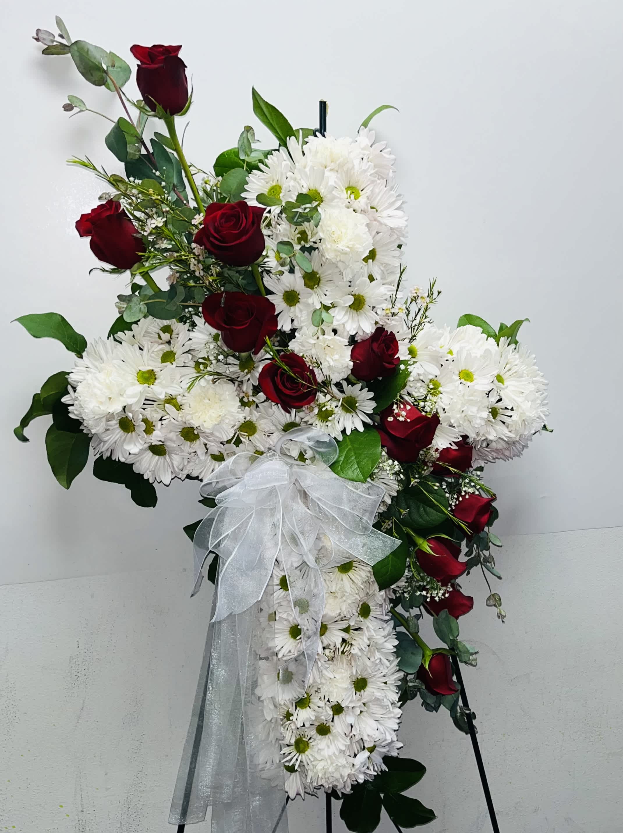 Cross-shaped floral spray with red roses and white daisies tied with a white bow