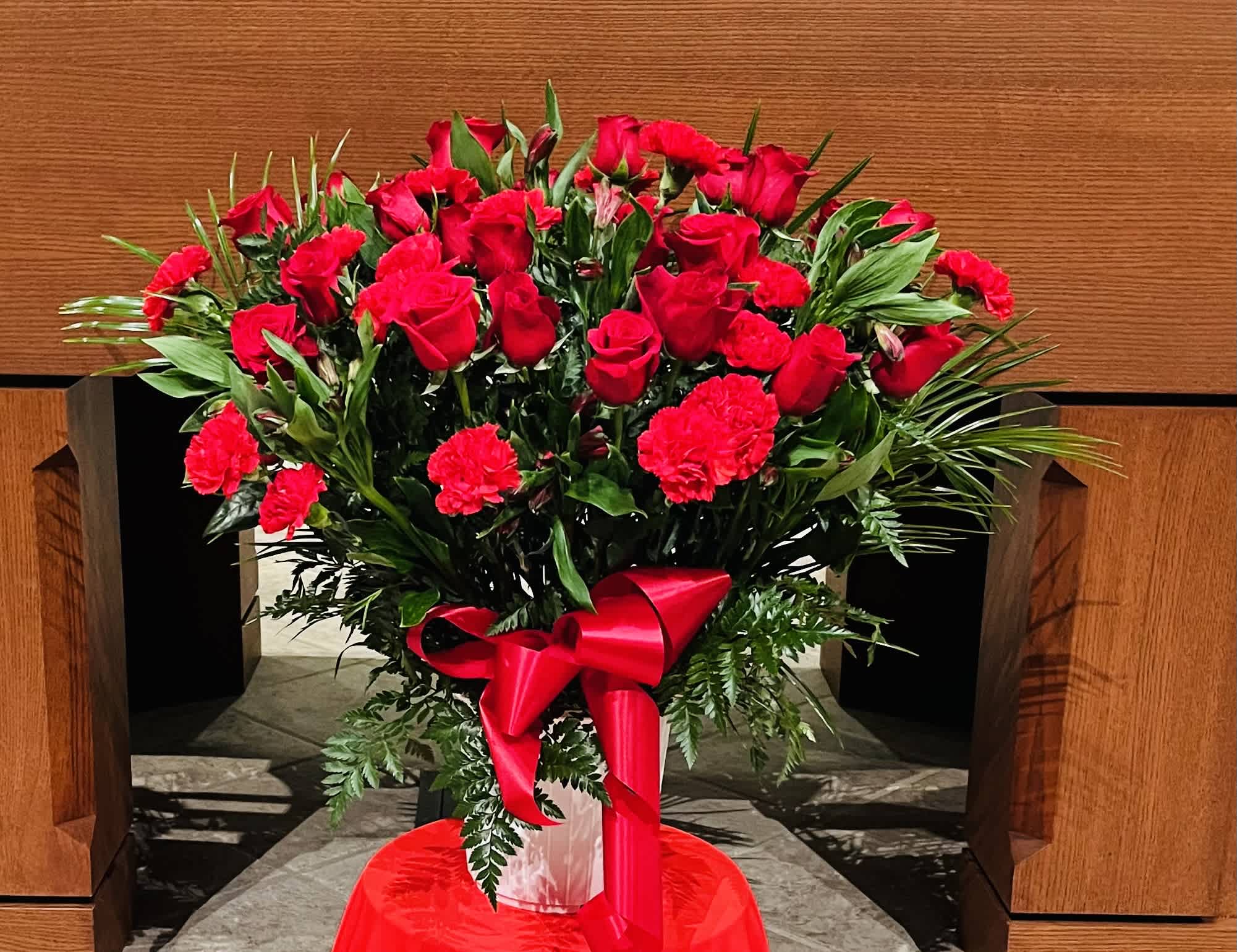 Red roses and carnations arranged in a vase with a red ribbon