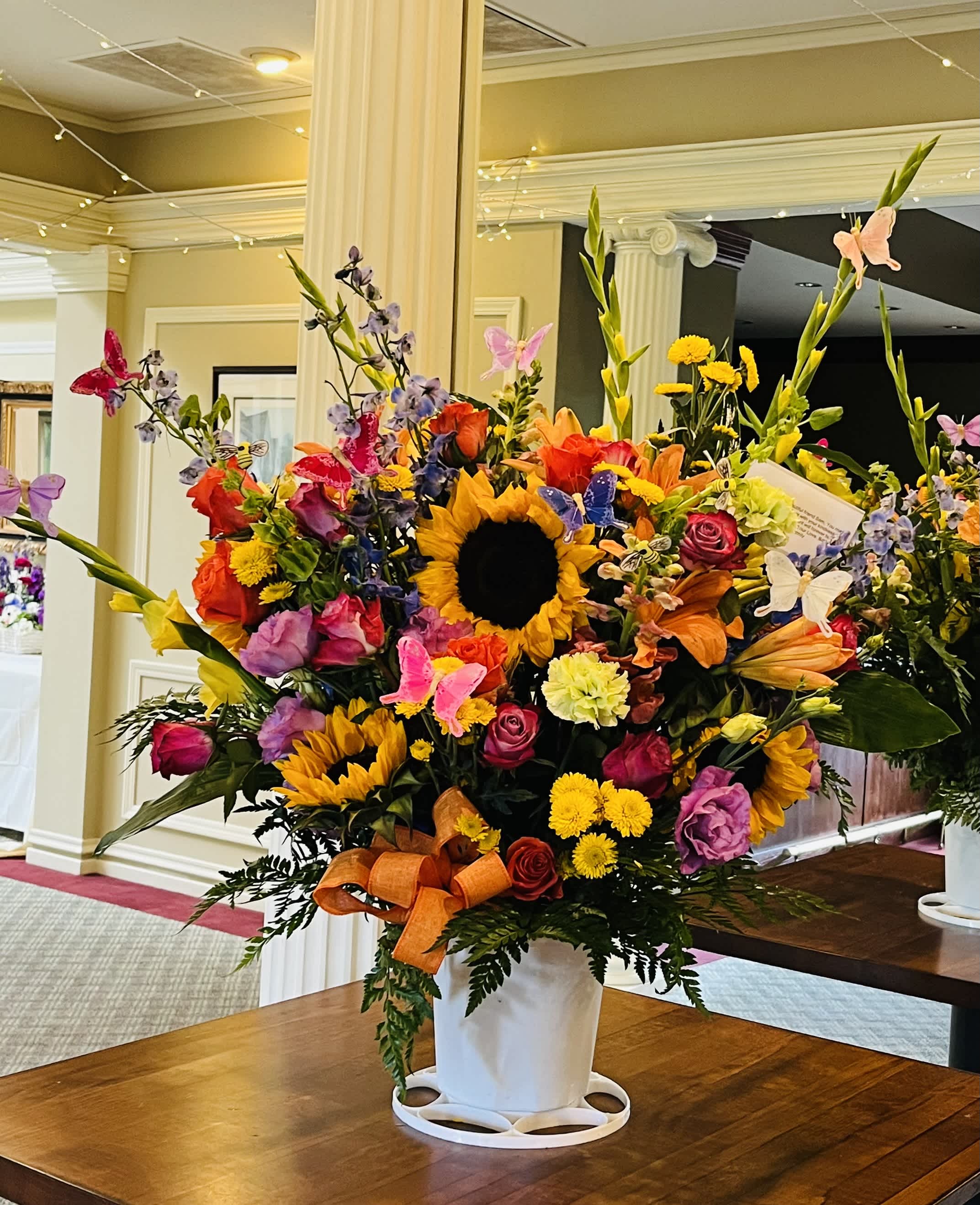 Large mixed flower arrangement with sunflowers and roses in a white vase