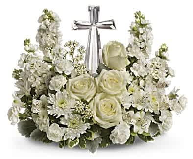 White floral arrangement with roses and stock around a silver cross