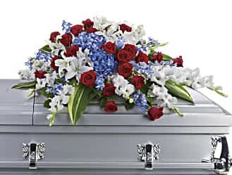 Red roses, white lilies, and blue flowers arranged on a silver casket