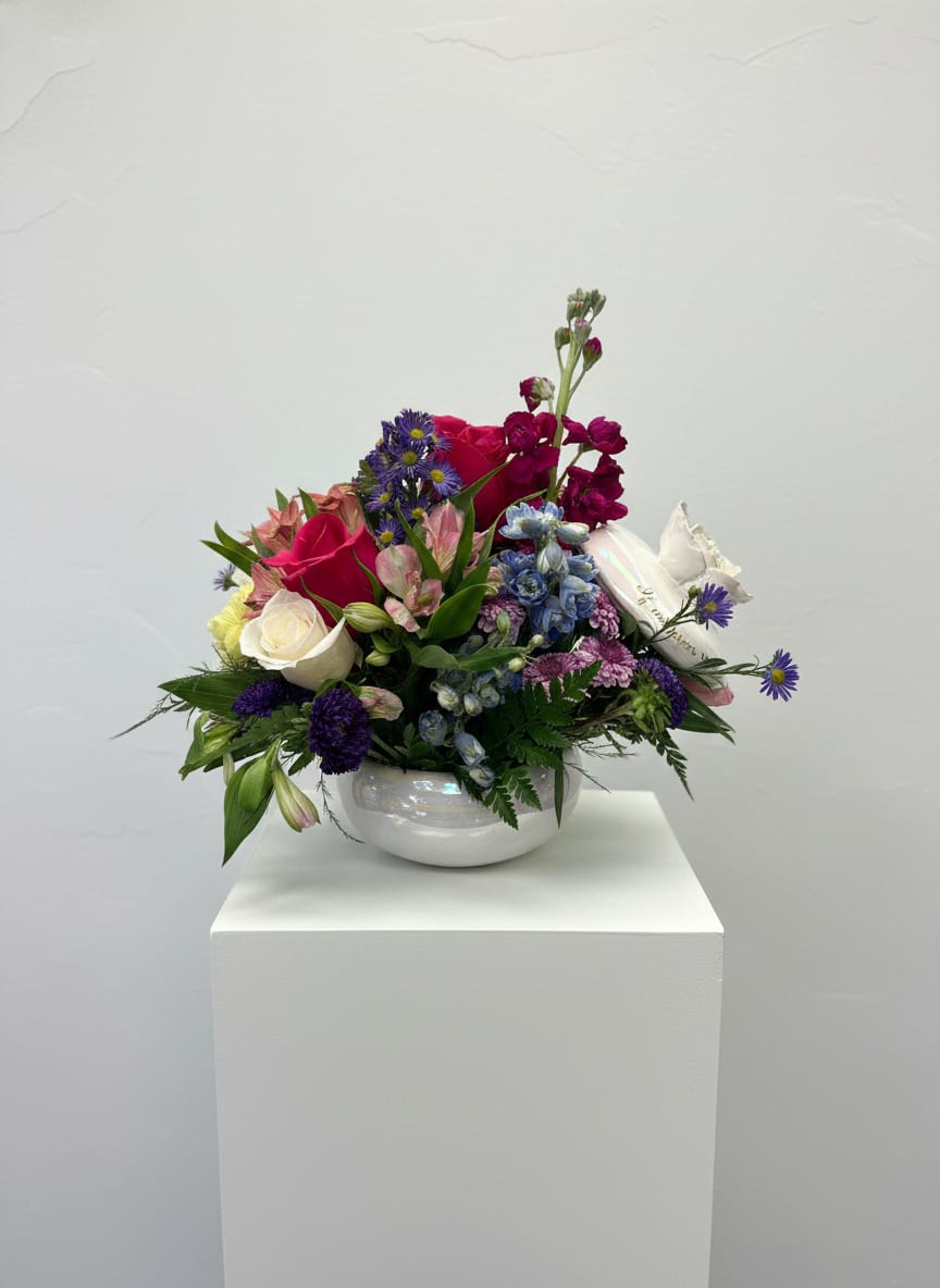 Keepsake  - Bright pink and white roses mingle with purple asters and soft pink alstroemeria in a low, garden-style flower arrangement made for cheerful gifting. This flower arrangement for birthdays, thank you gestures, or spring celebrations sits in a glossy white ceramic bowl vase, giving the person you're thinking of a joyful, romantic-but-playful display that feels both elegant and approachable.  The Keepsake arrangement is a dense, outward-spreading composition of roses, lilies, carnations, alstroemeria and asters in mixed color tones-pink, purple, white and touches of blue-creating layered color and texture without standing tall. The glossy white bowl keeps the design intimate and full, perfect for tabletops, desks, or a kitchen counter where the blooms can be admired up close.  Give this as a bright everyday bouquet that makes someone feel genuinely celebrated; it's the kind of arrangement that reads as thoughtful whether it marks a birthday, an expression of thanks, or simply because you were thinking of them. Includes the white ceramic bowl vase and arrives ready to display - no extra arranging required.