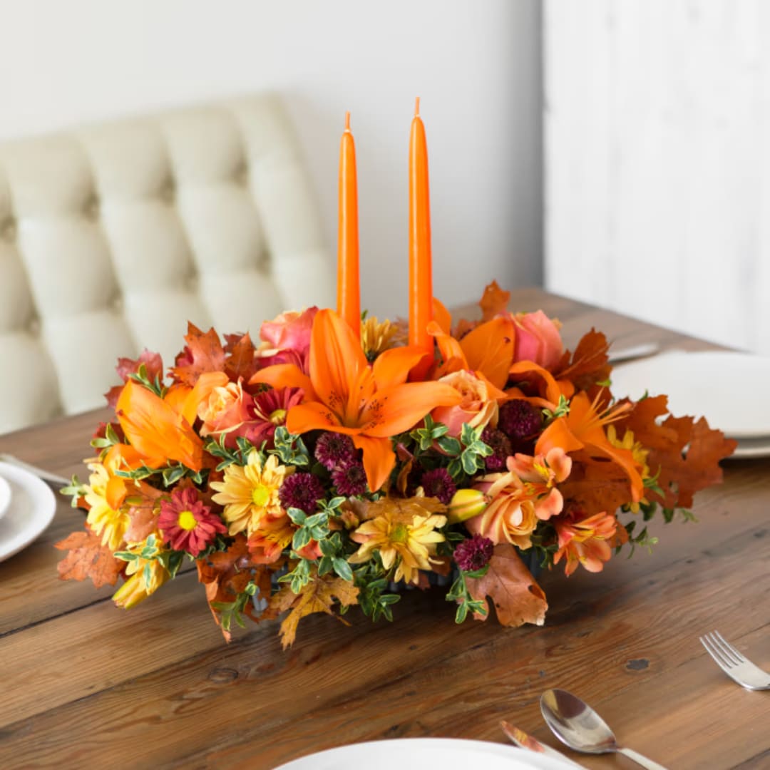 Orange floral centerpiece with two tall candles on a dining table