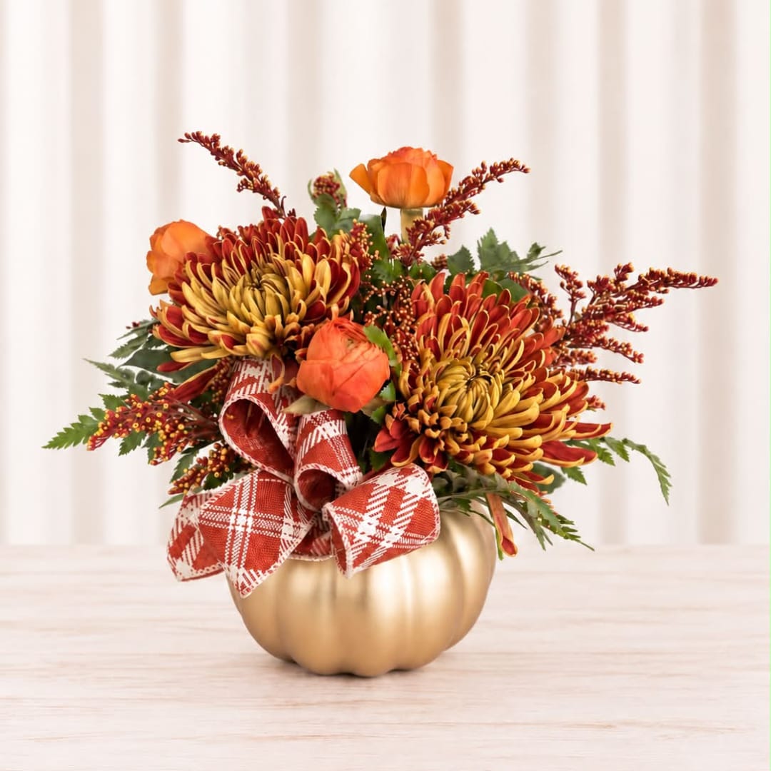 Orange and burgundy floral arrangement in a gold pumpkin container with plaid ribbon