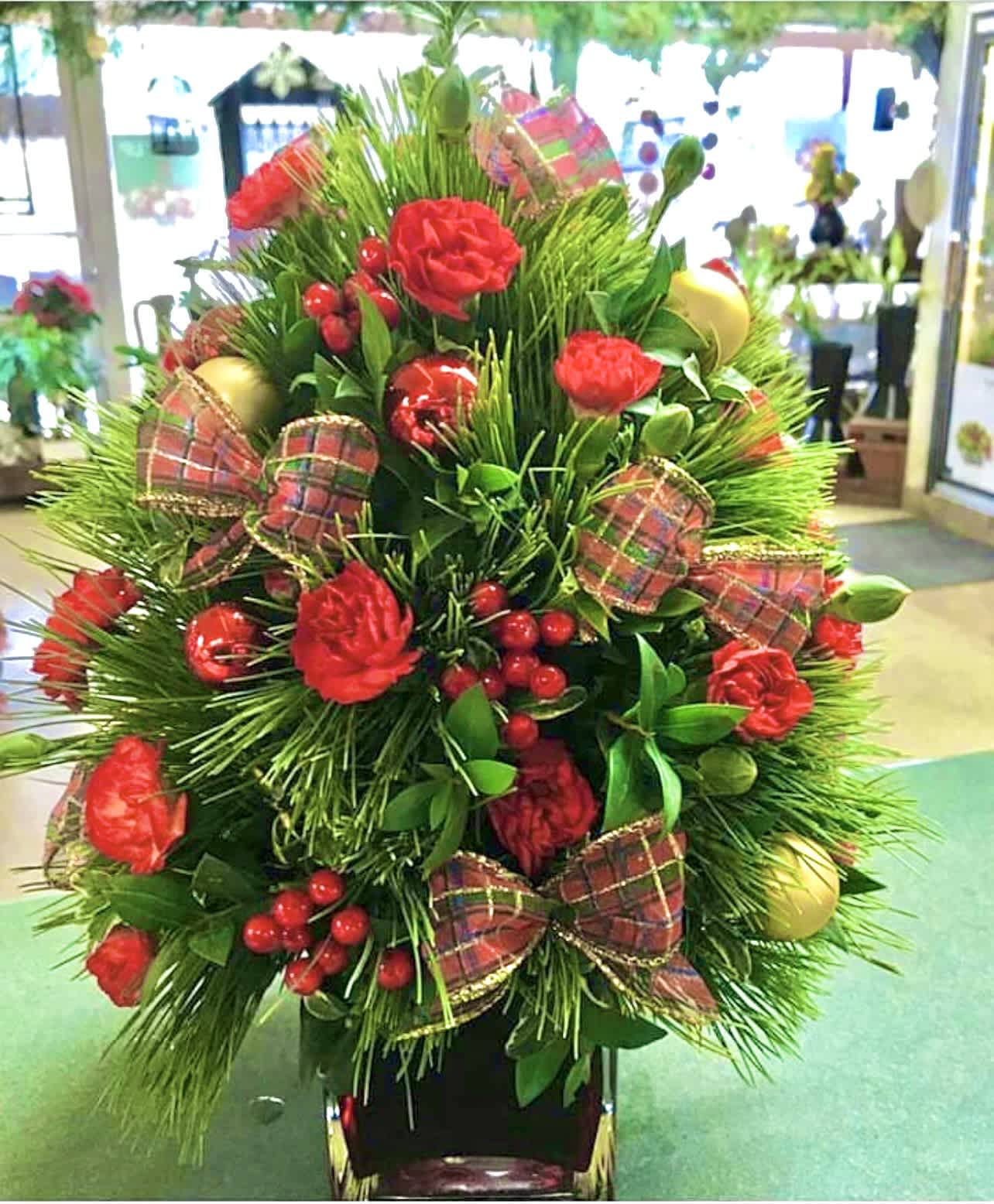18" Mini Christmas Tree - Mixture of Fresh Christmas greens, mini carnations, ornaments, berries and bows. About 18"  in height and perfect for any table top or desk. Greens and ribbon are subject to change depending on availability. 