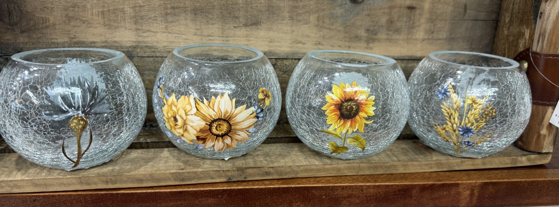 Four crackled glass bowls with painted floral designs on a wooden shelf