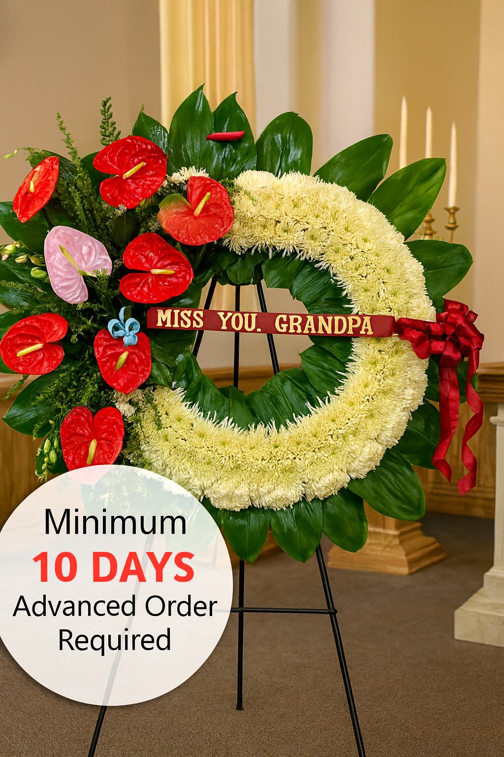 Large white sympathy wreath with red and pink flowers on a stand and a ribbon reading 'Miss you, Grandpa'