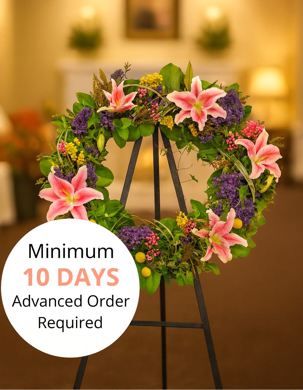 Standing wreath with pink lilies and mixed purple and yellow flowers on a black easel.