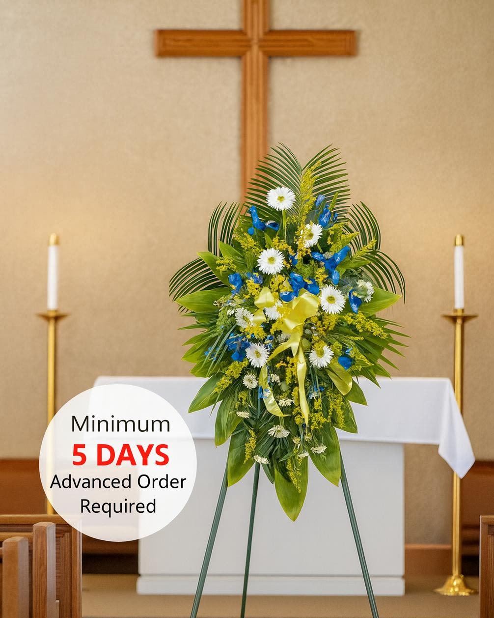 Standing funeral spray of white and blue flowers with yellow ribbon on an easel in a church sanctuary