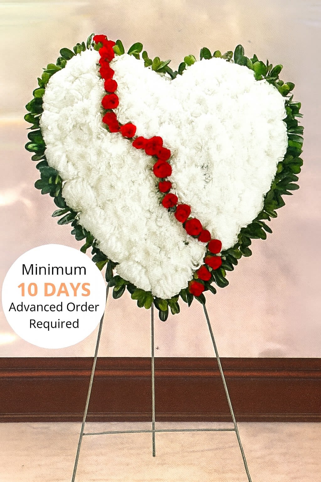 Heart-shaped white funeral wreath with red flowers on a metal stand