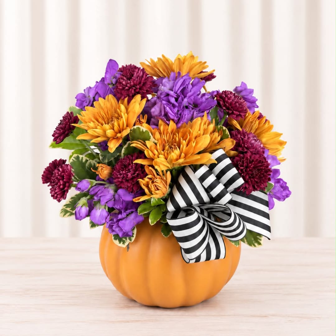 Purple and orange flower arrangement in a pumpkin container with a striped bow