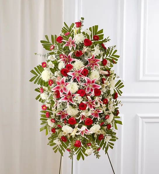 Red Rose And Lily Standing Spray - Celebrate a beautiful life with a truly heartfelt gesture. Our elegant standing sympathy spray is arranged with a gathering of radiant red, soft pink and pure white blooms. A traditional floral display for the services, it’s a touching way to honor the memory of a loved one while expressing your deepest condolences.One-sided standing spray arrangement with red roses and Matsumoto asters, pink Stargazer lilies, white Peruvian lilies (alstroemeria), carnations and football mums; accented with spiral and seeded eucalyptus, baby’s breath and assorted greenery