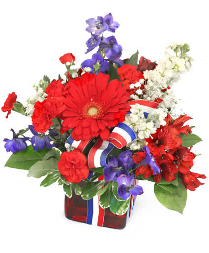 Red, white, and blue floral arrangement in a red glass vase with ribbon