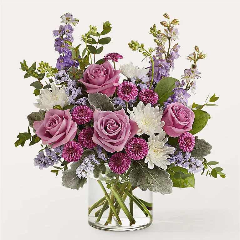 Pink roses and purple-white mixed flowers in a clear glass vase
