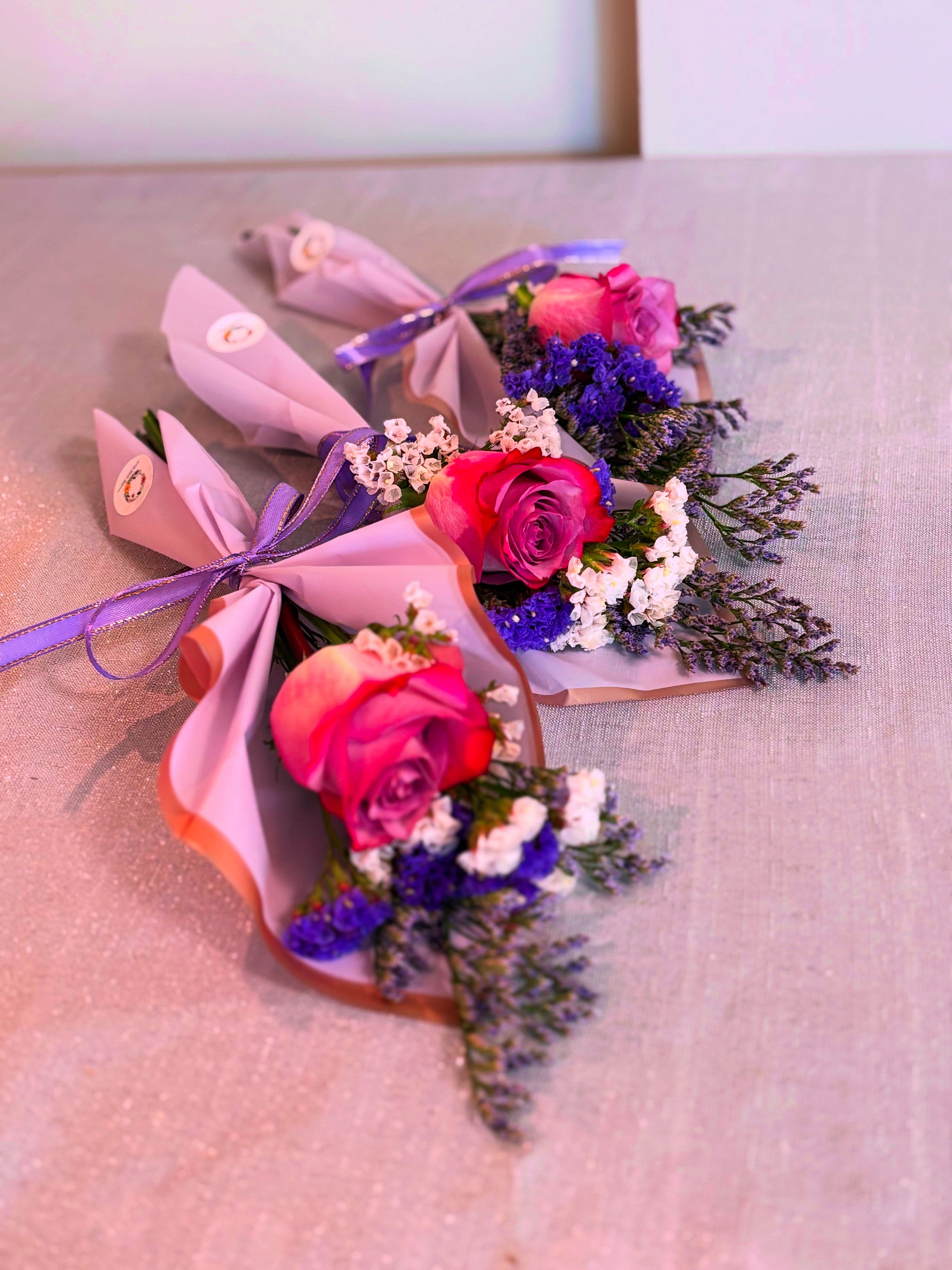 Three small pink rose bouquets wrapped in pastel paper with purple ribbon