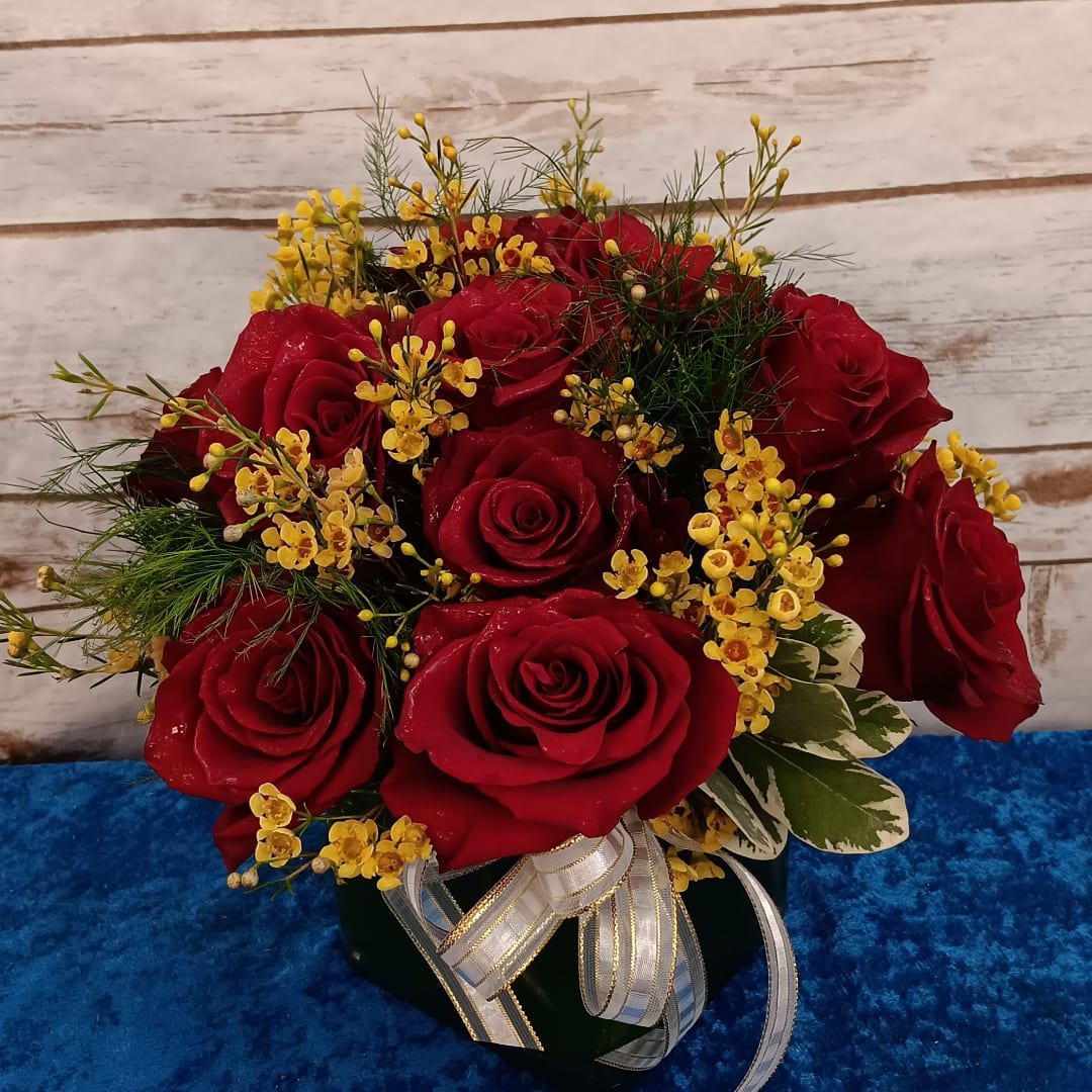 Red roses with small yellow filler flowers in a dark vase with ribbon