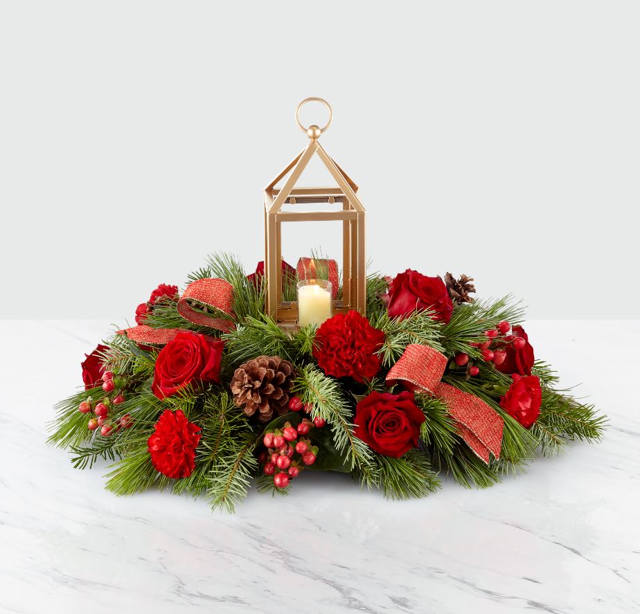 I’LL BE HOME FOR CHRISTMAS™ CENTERPIECE - Create a festive centerpiece worth gathering around. Beautiful seasonal blooms surround a matte gold lantern with a glass insert that perfectly dresses up any holiday table.