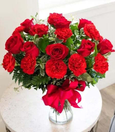Bouquet of red roses and carnations in a glass vase with a red ribbon