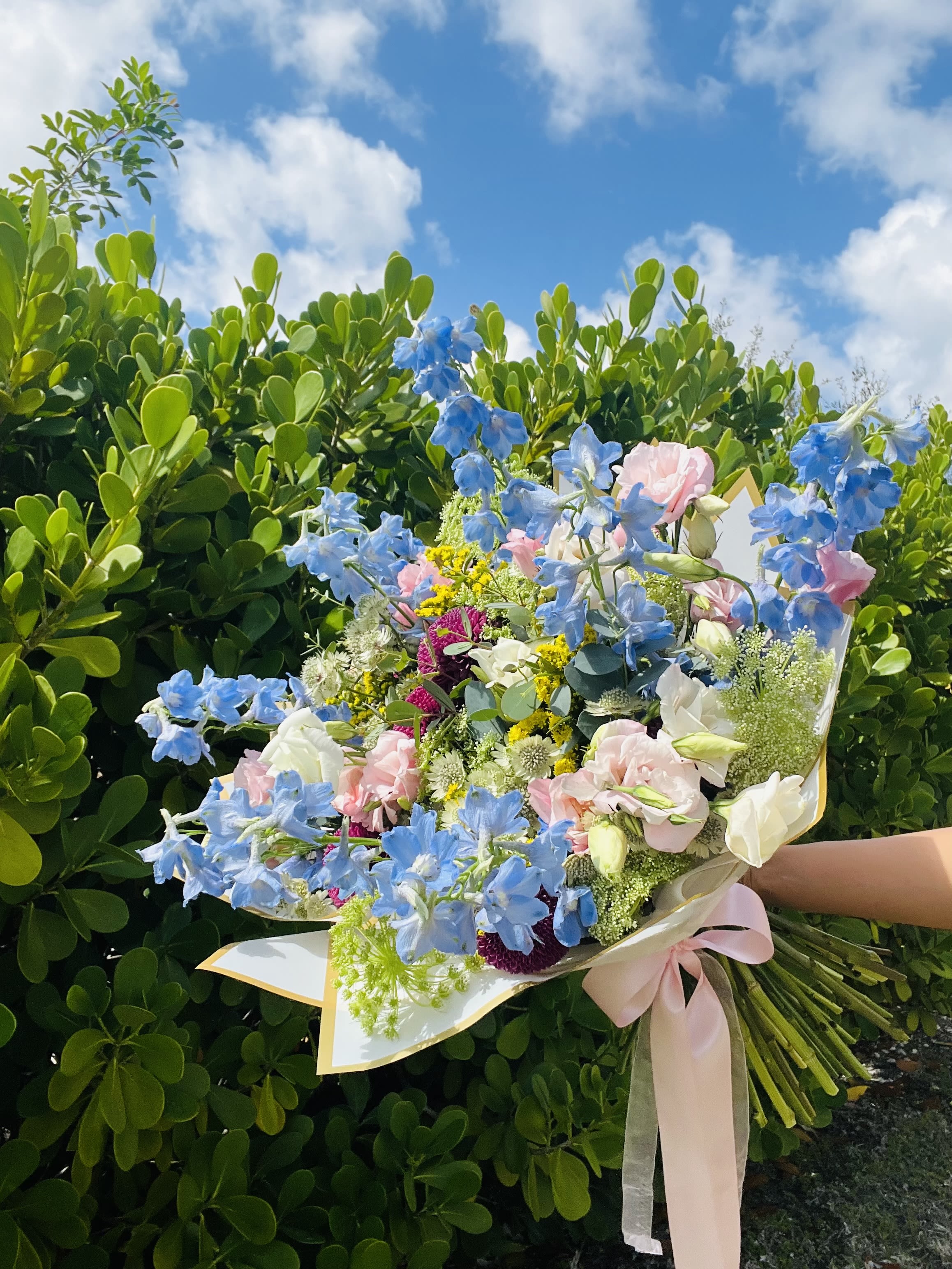 Sky Garden - Sky Garden is a dreamy, garden-style bouquet inspired by open skies and blooming fields. Featuring soft blue delphinium, delicate blush florals, crisp whites, and vibrant seasonal accents, this arrangement is full of movement, texture, and natural beauty.  Its airy design and layered colors create a bouquet that feels both elegant and full of life — perfect for special occasions, celebrations, or making a statement with something truly unique.  Because we work with fresh, seasonal flowers, each bouquet is thoughtfully designed using the best blooms available at the time. While the color palette and overall style will remain consistent, the exact flowers may vary — making every arrangement uniquely beautiful.