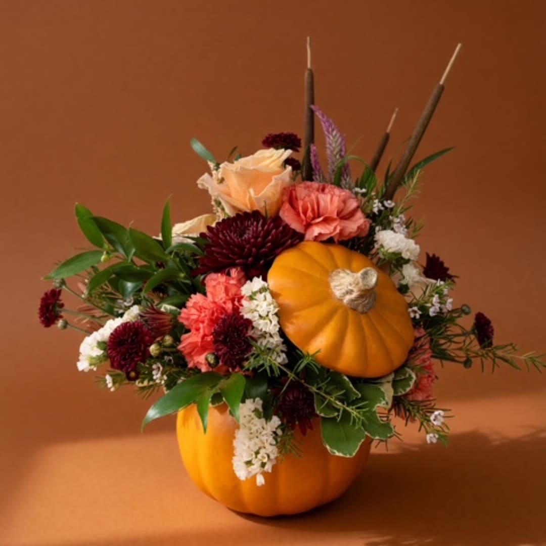 Autumn floral arrangement in two orange pumpkins with peach, burgundy, and white flowers