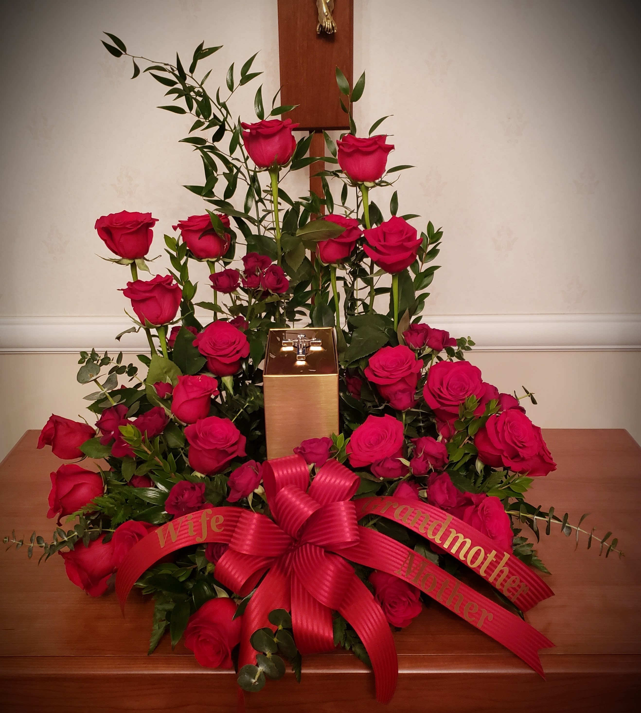 Roses of Love Urn Ring by The Potted Plant - An elegant creation of red roses surrounding the memorial urn of your loved one.  Arranged in a crowning display and complimented with deep green italian ruscus, spiral eucalyptus, myrtle and fern. This creation can be done in most colors. 