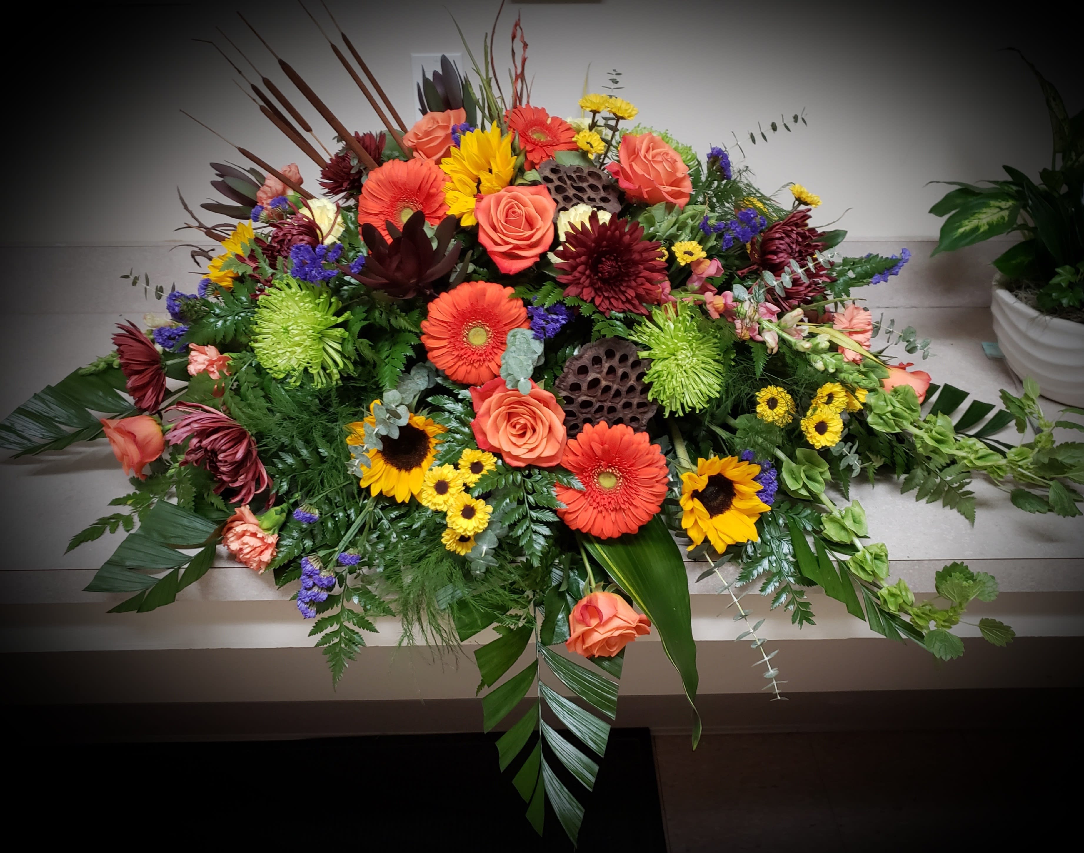 Large colorful floral casket spray with roses, gerbera daisies, and sunflowers