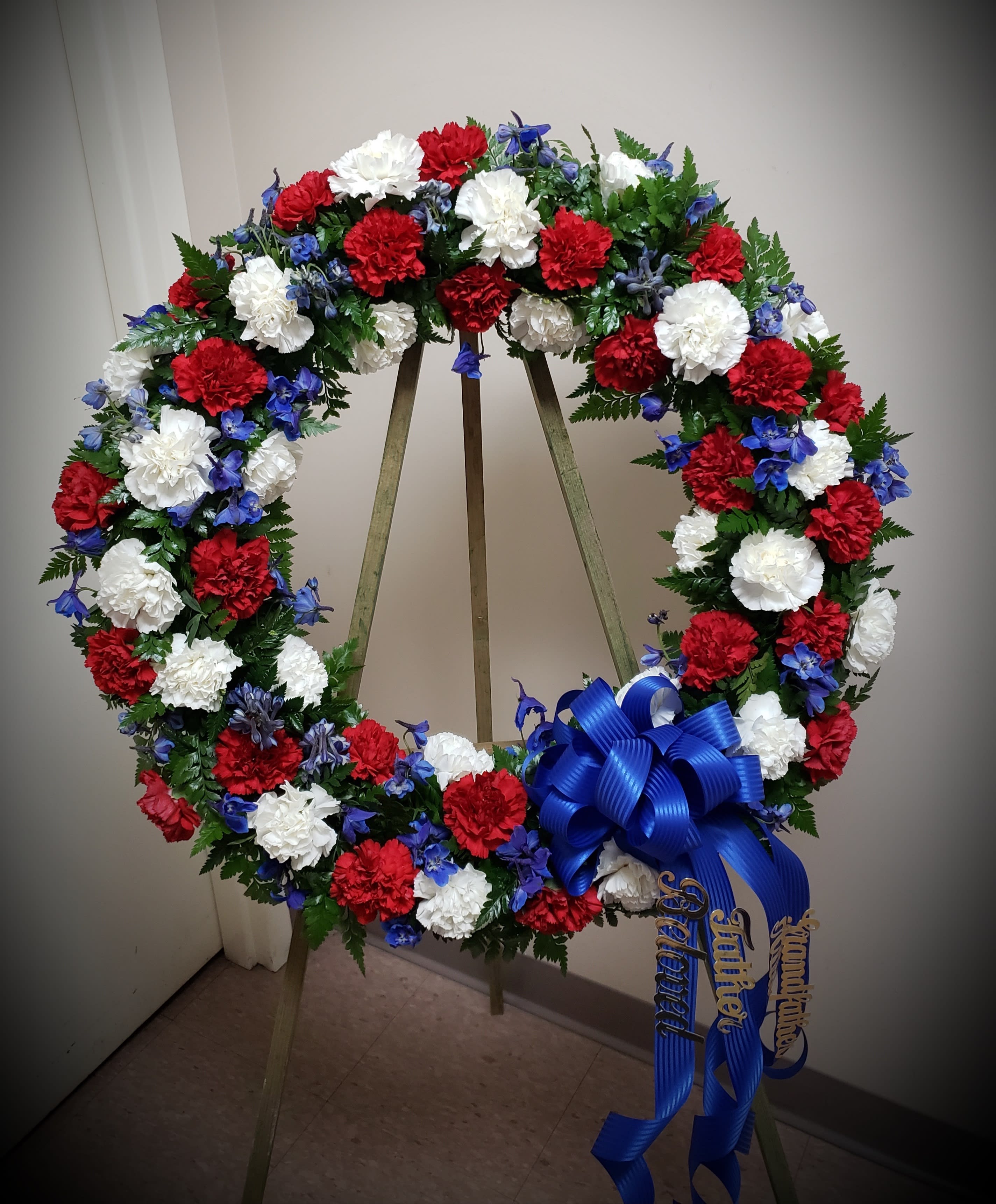Red, white, and blue floral wreath on a stand with a ribbon bow