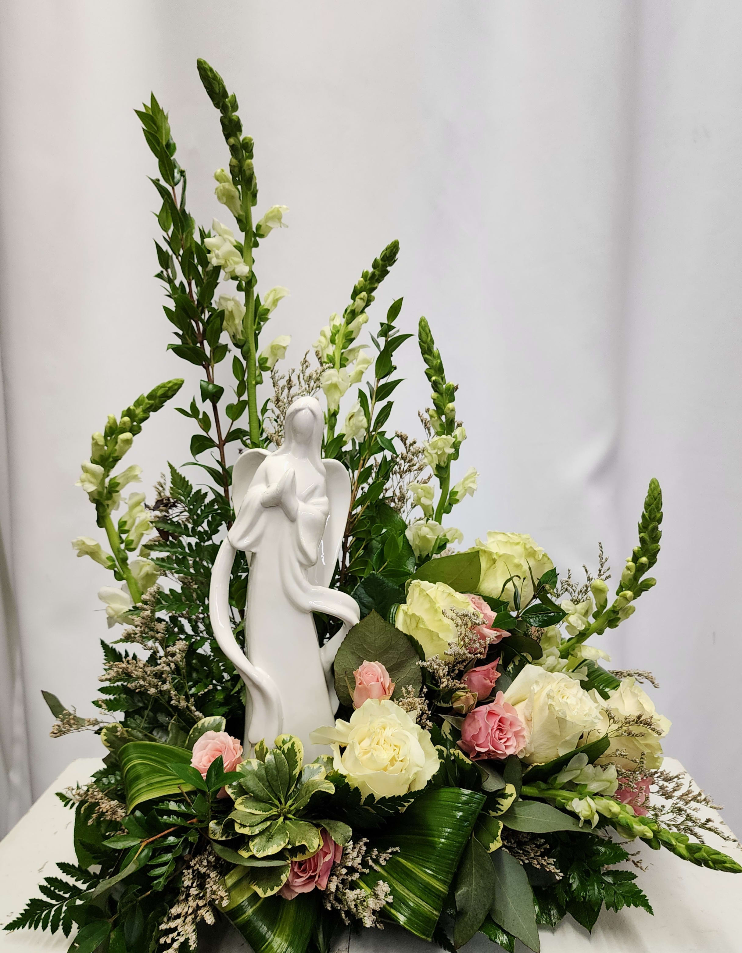 White angel figurine surrounded by cream and pink roses in a floral arrangement