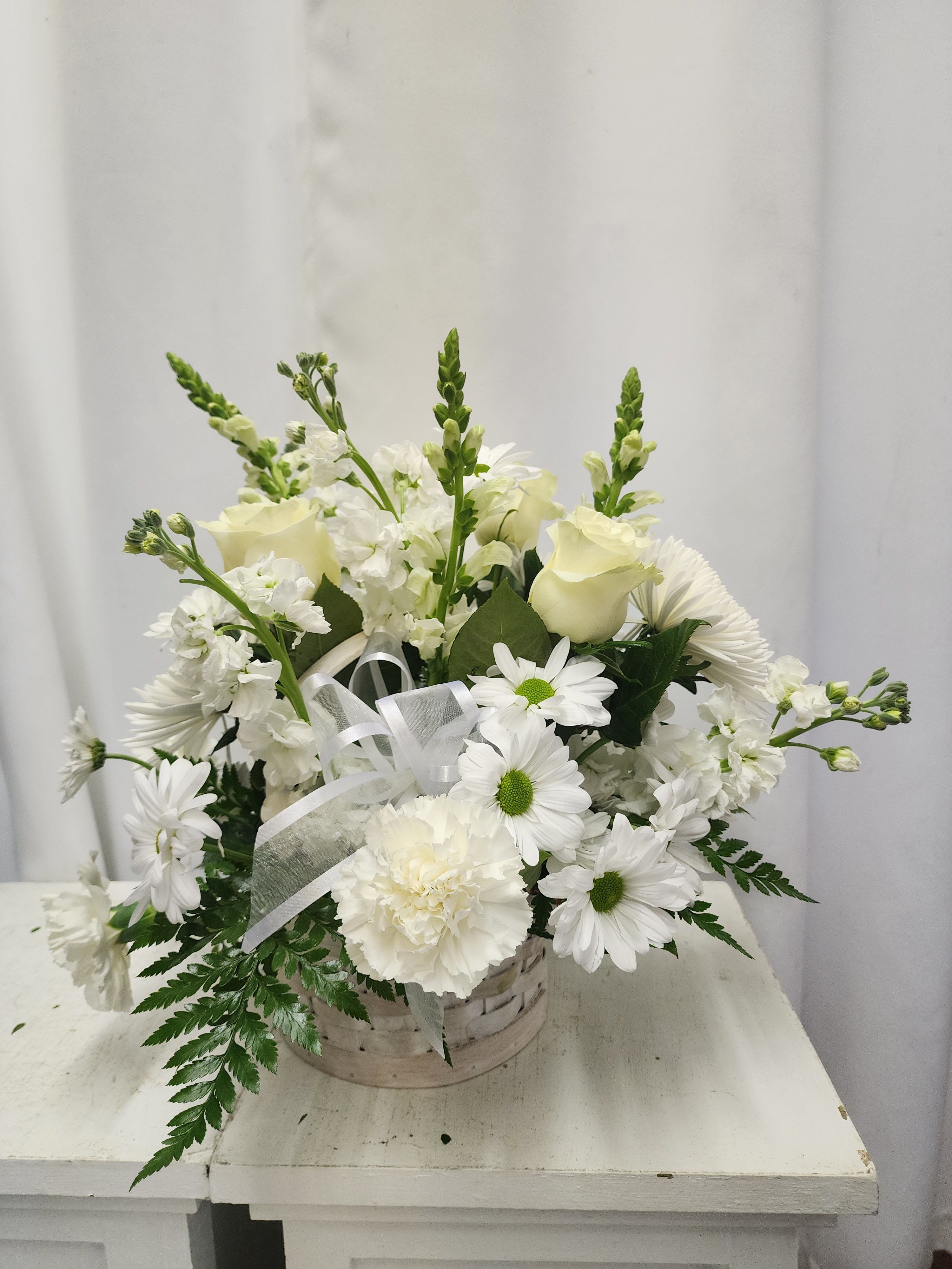 White floral arrangement in a basket with ribbon