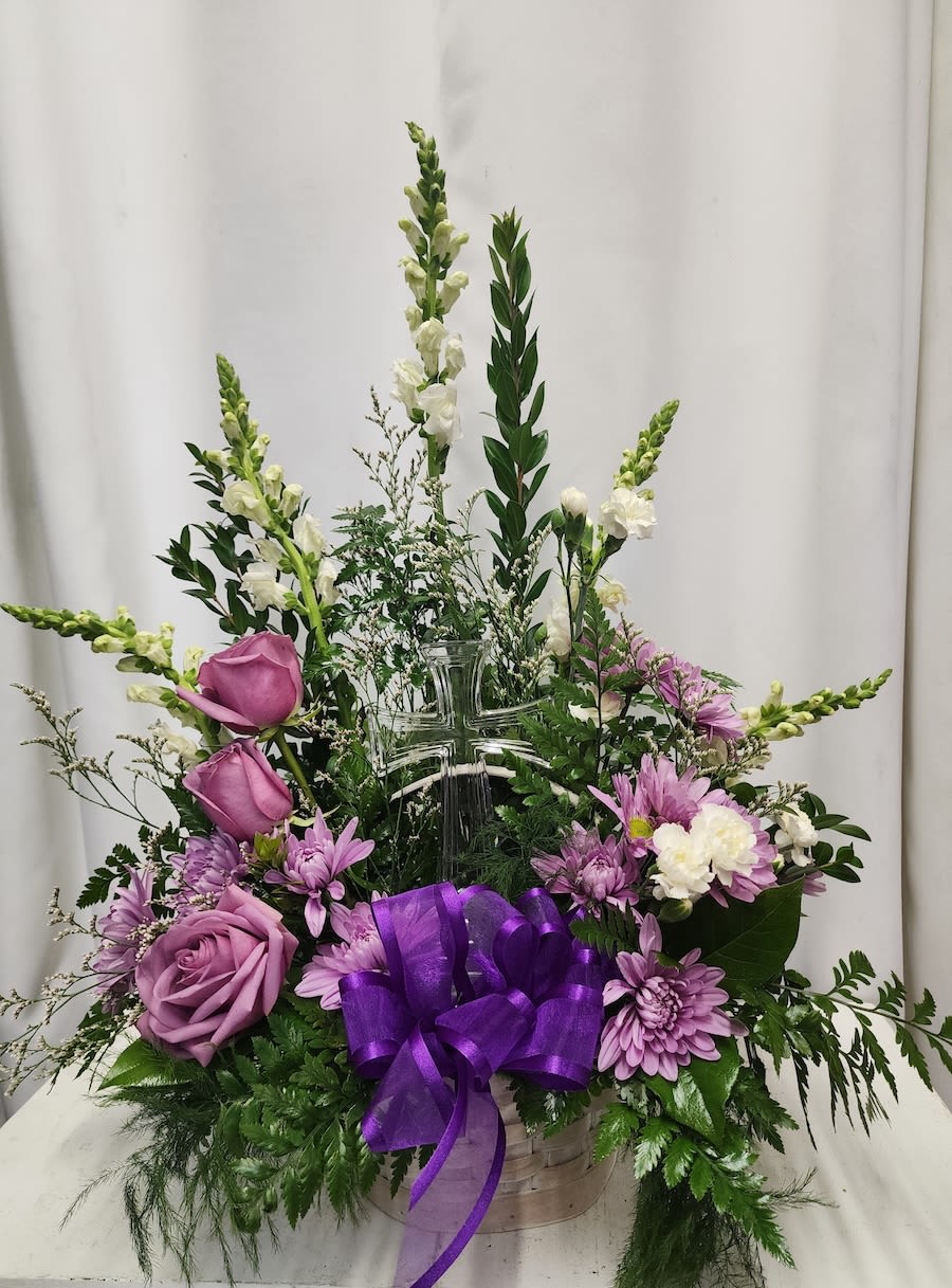Purple and white floral arrangement in a clear cross vase with a purple ribbon