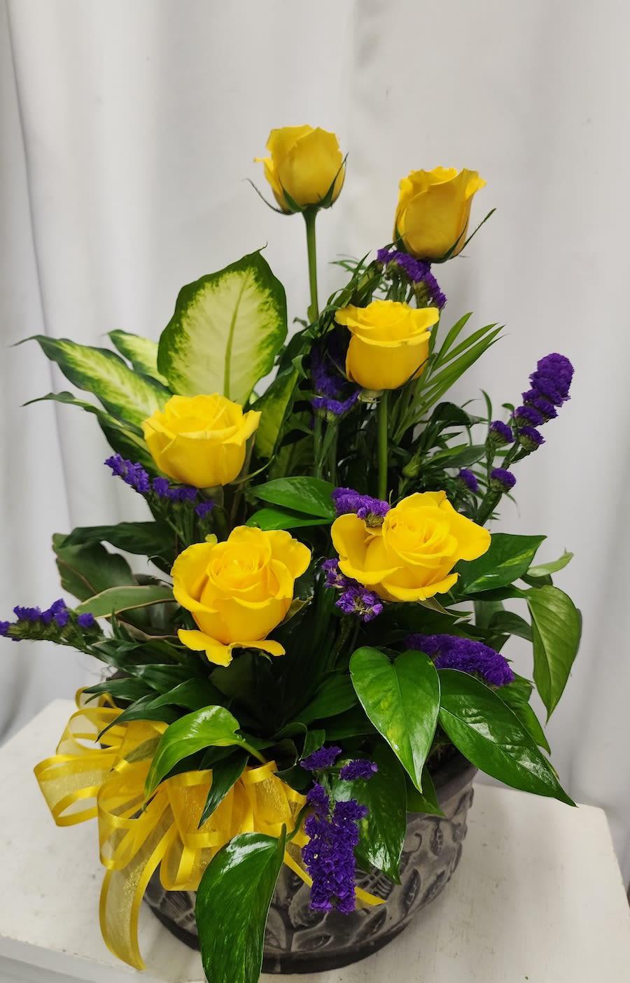Yellow roses and purple filler flowers arranged in a decorative vase