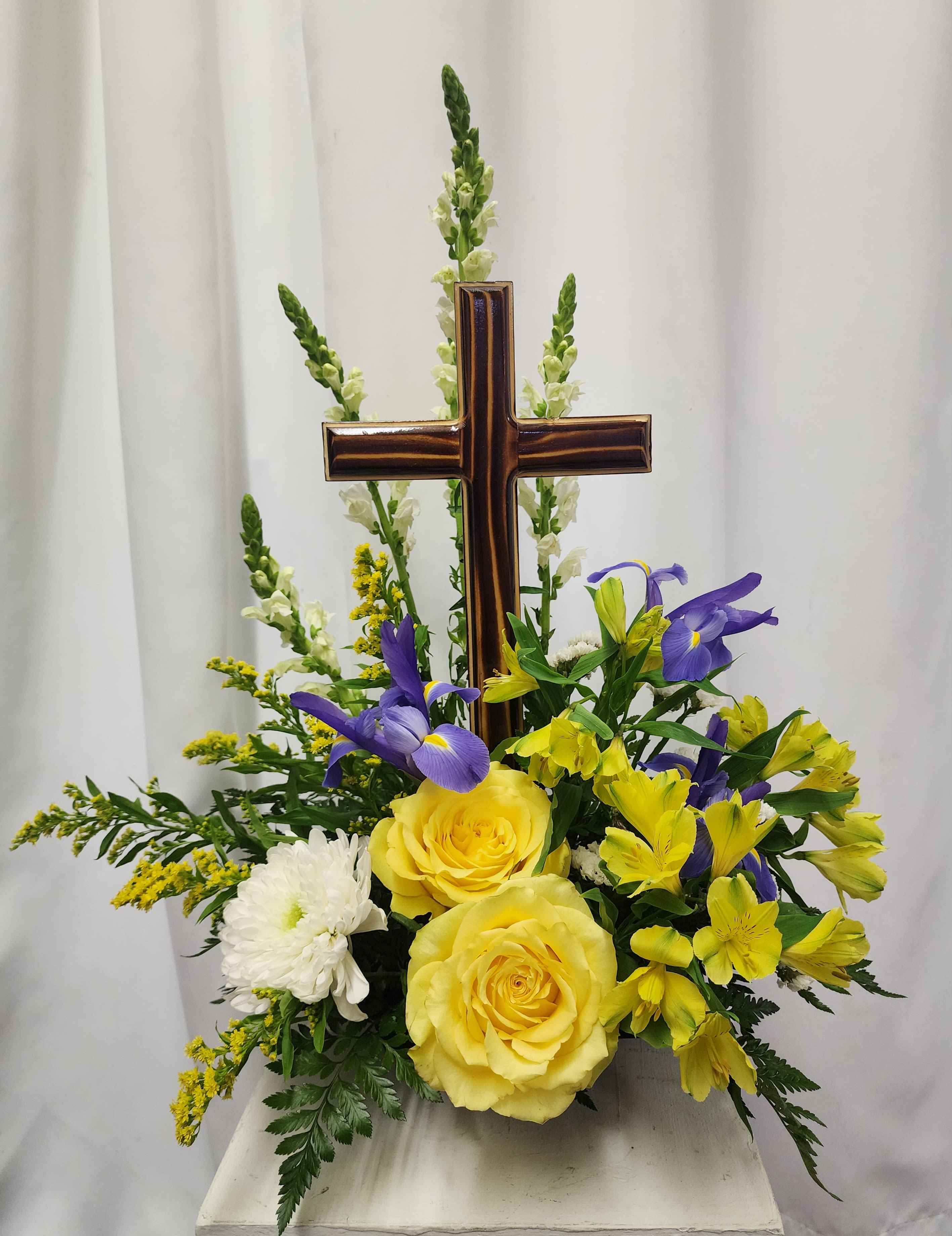 Yellow roses and purple flowers arranged around a wooden cross