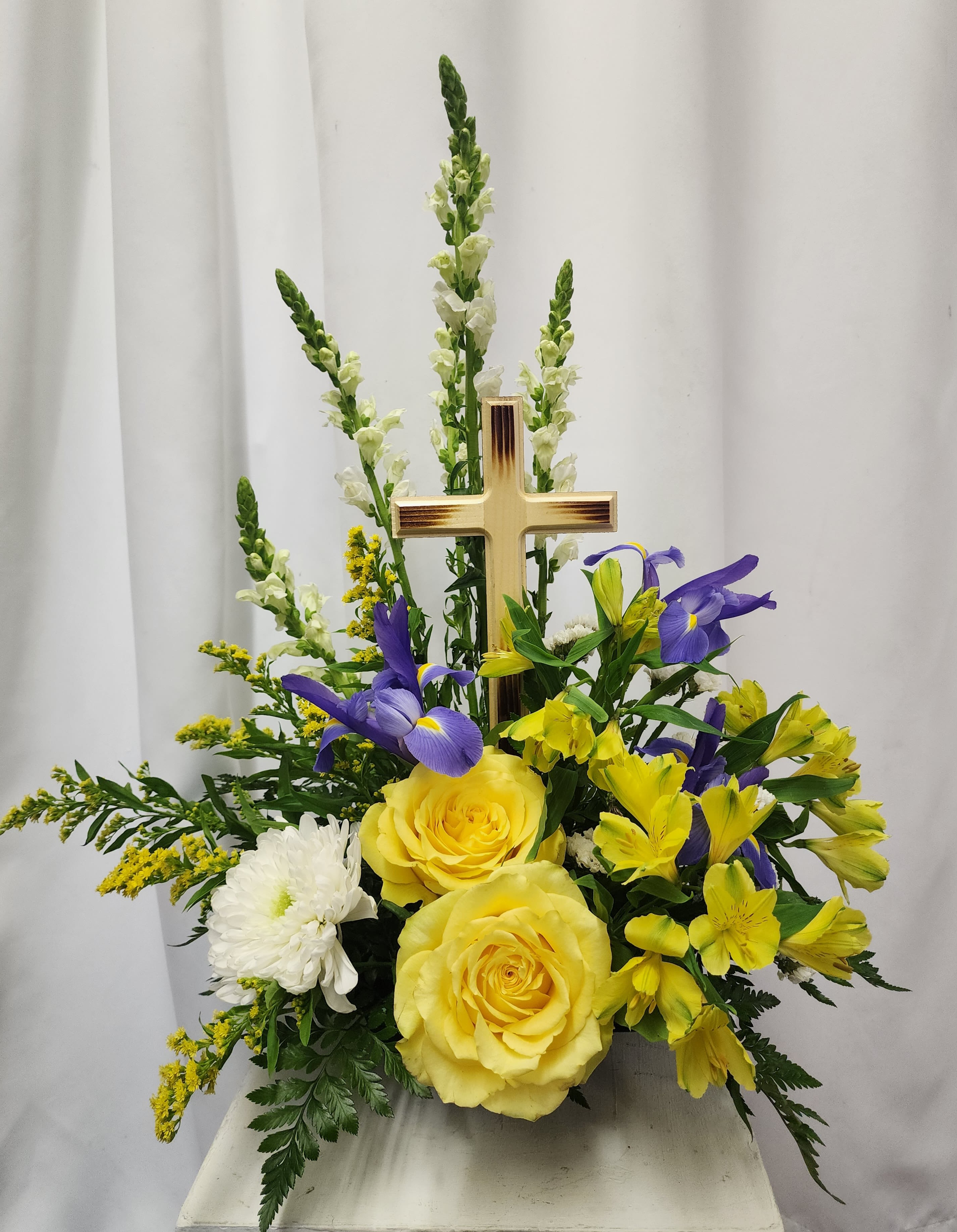 Yellow roses and purple flowers arranged around a gold cross