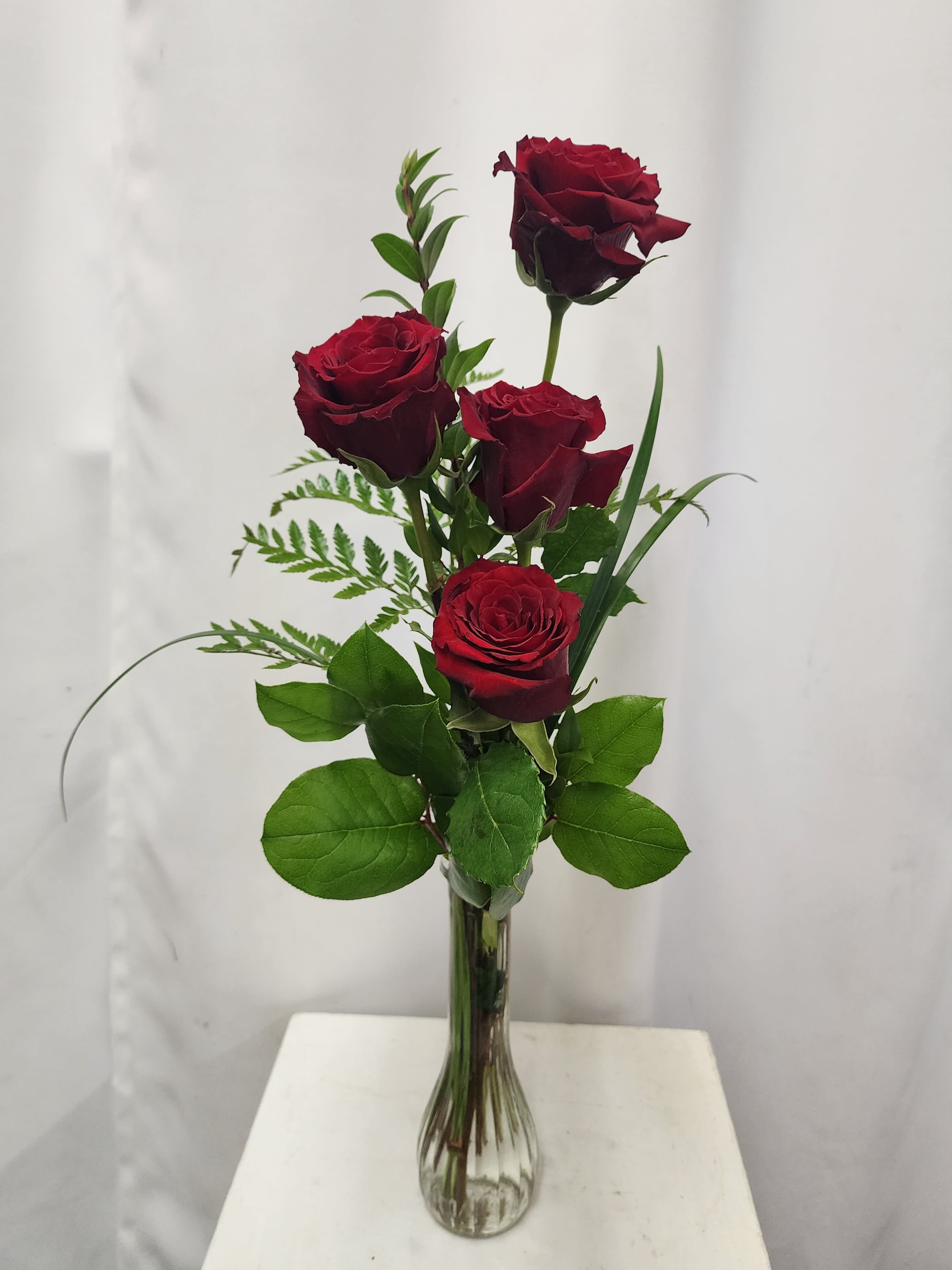 Four red roses in a clear glass vase with greenery