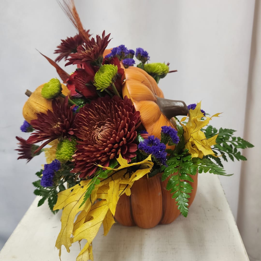 Autumn floral arrangement in a pumpkin-shaped container with burgundy and purple blooms