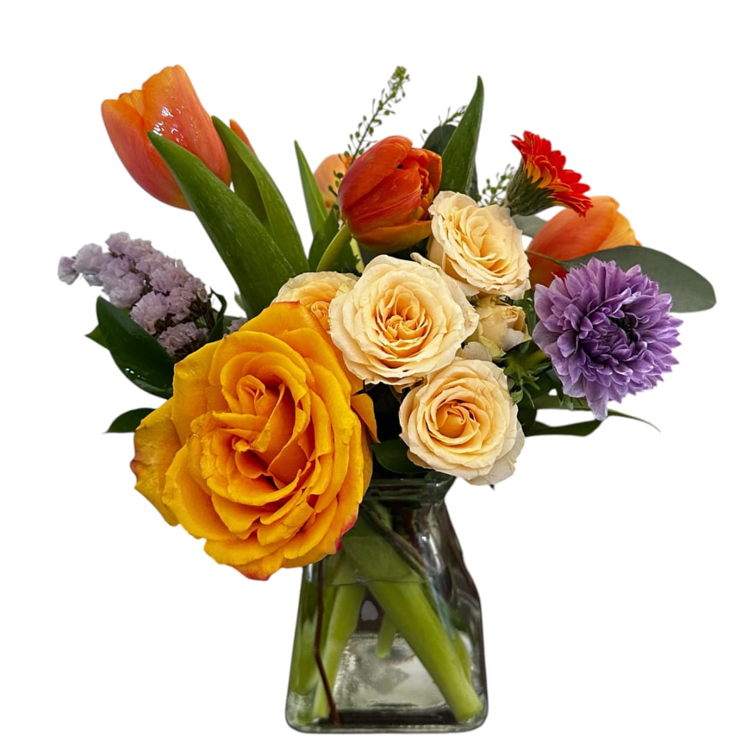 Mixed bouquet of orange, yellow, cream, and purple flowers in a glass vase