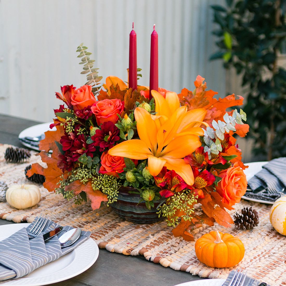 Autumn floral centerpiece with orange lilies, roses, and red candles in a low bowl