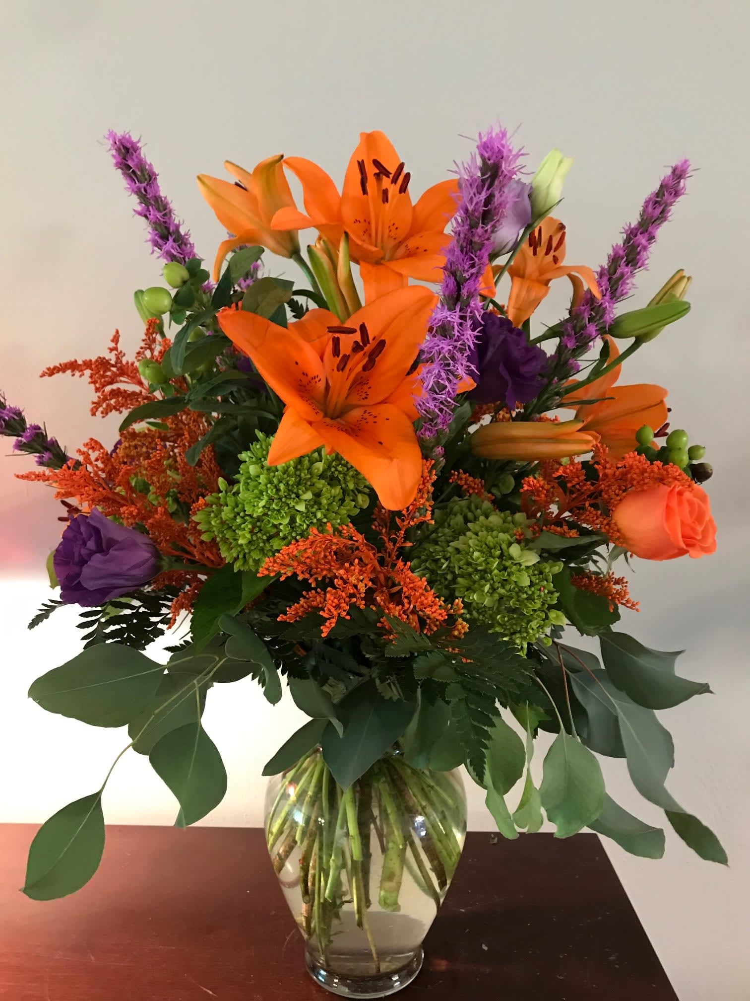 Orange lilies and purple flowers in a glass vase