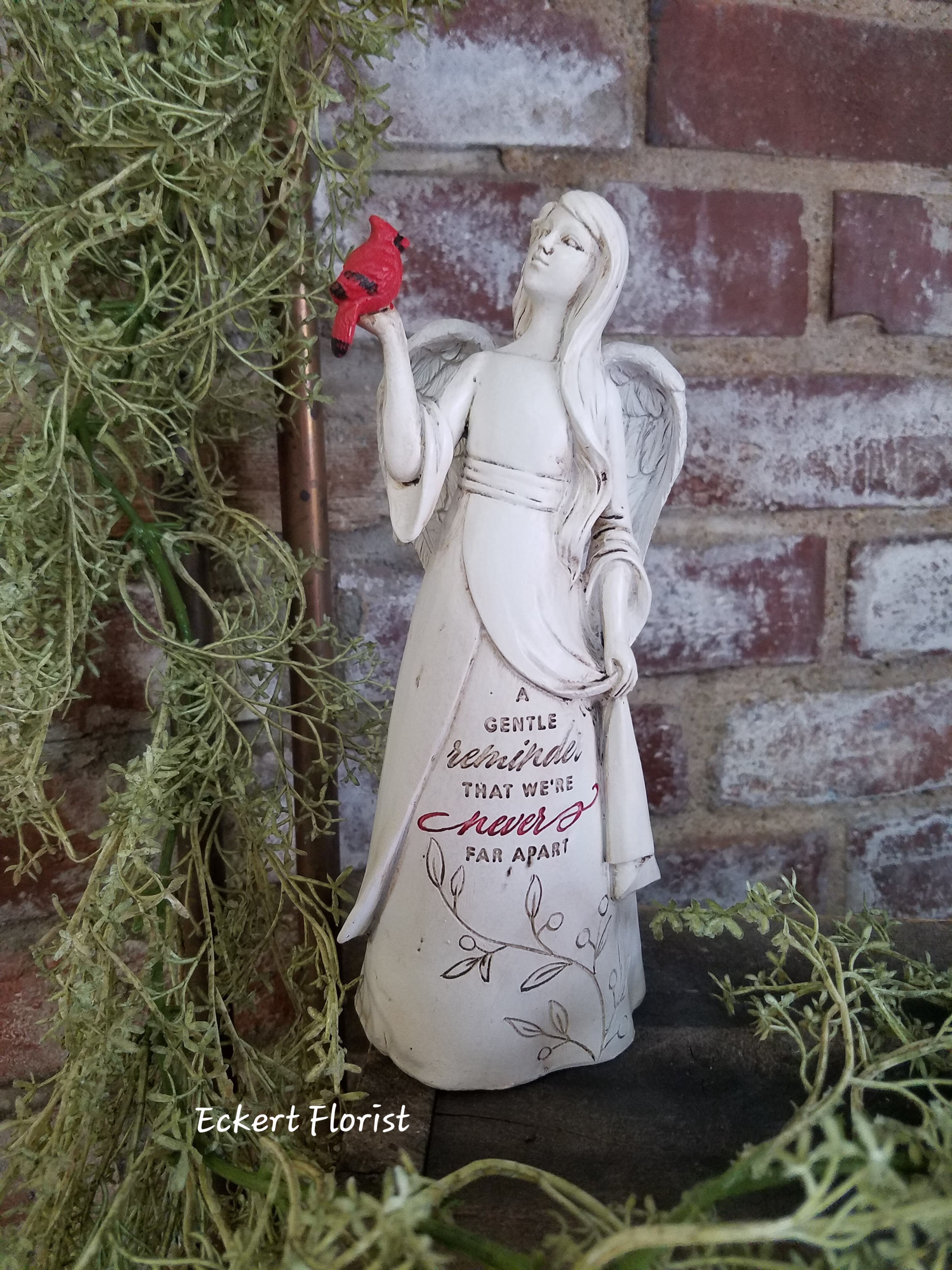 Angel figurine holding a red bird beside trailing greenery
