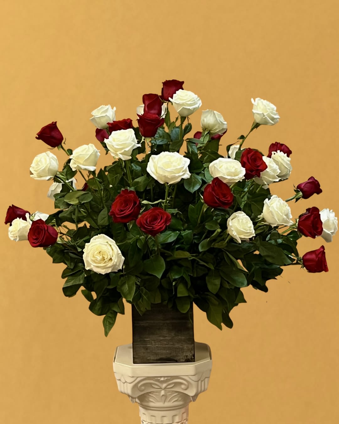 Red and white roses arranged in a tall vase on a pedestal
