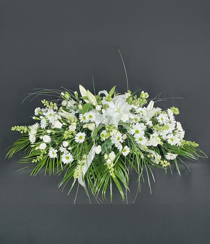 Elongated white lily and daisy spray with trailing palm fronds on a dark background