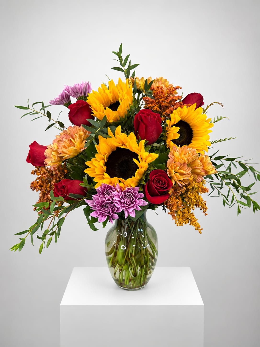Bouquet of sunflowers, red roses, and purple mums in a glass vase