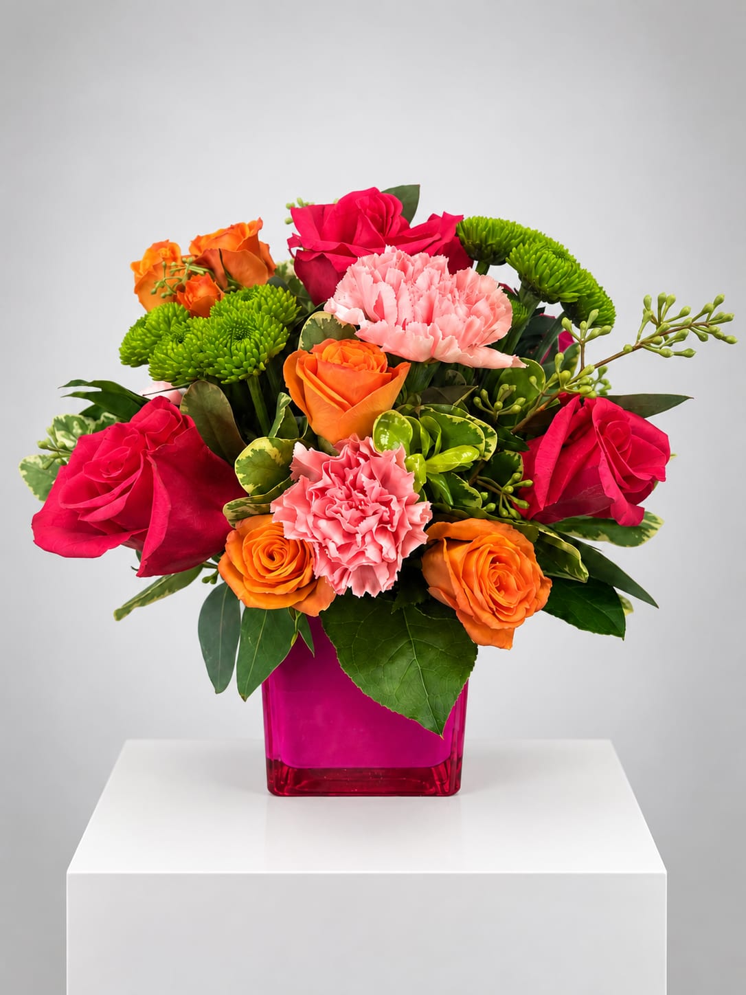 Bright mixed bouquet of roses, carnations, and green mums in a pink vase